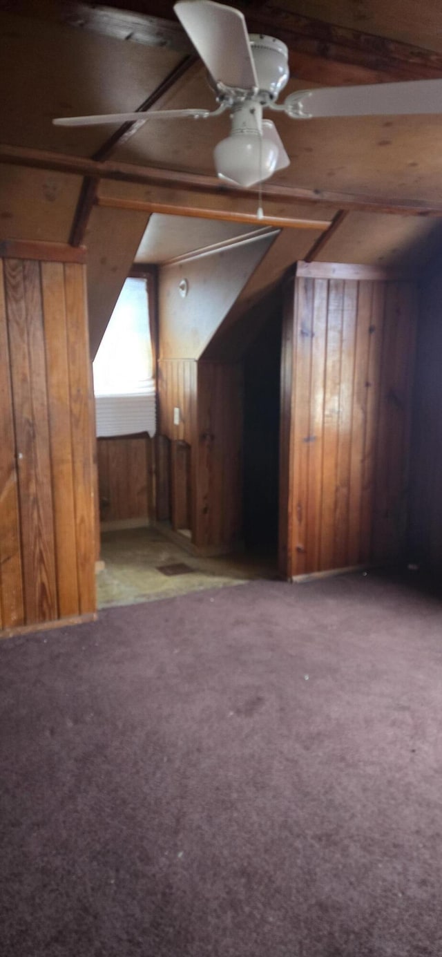 additional living space featuring ceiling fan, lofted ceiling, carpet flooring, and wooden walls