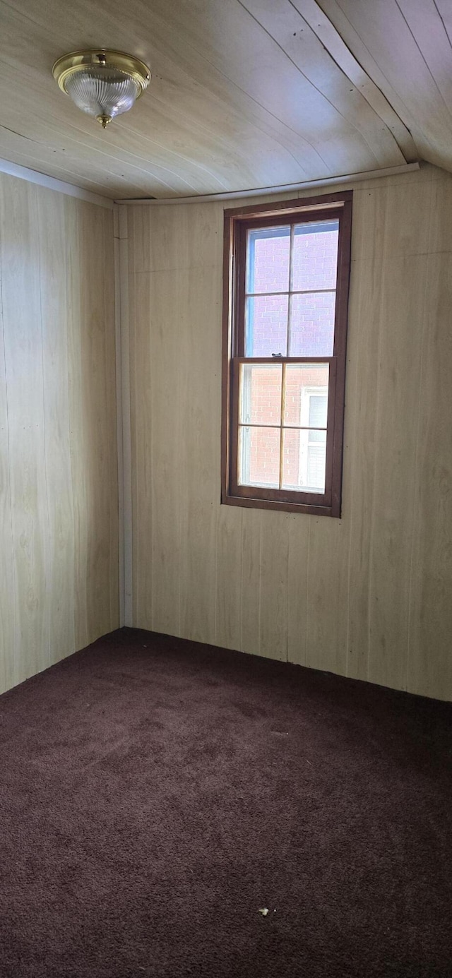 carpeted empty room featuring wooden ceiling and wood walls