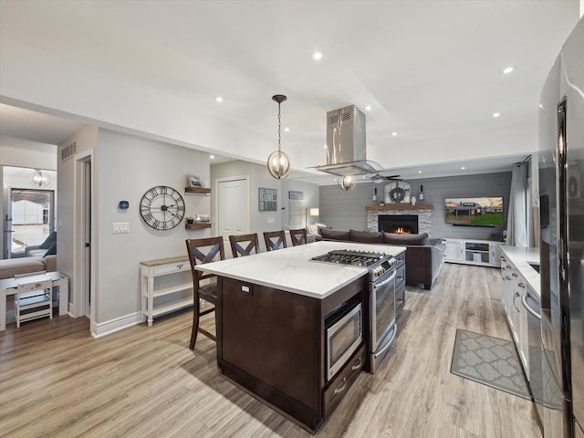 kitchen with pendant lighting, appliances with stainless steel finishes, island exhaust hood, a center island, and a kitchen bar