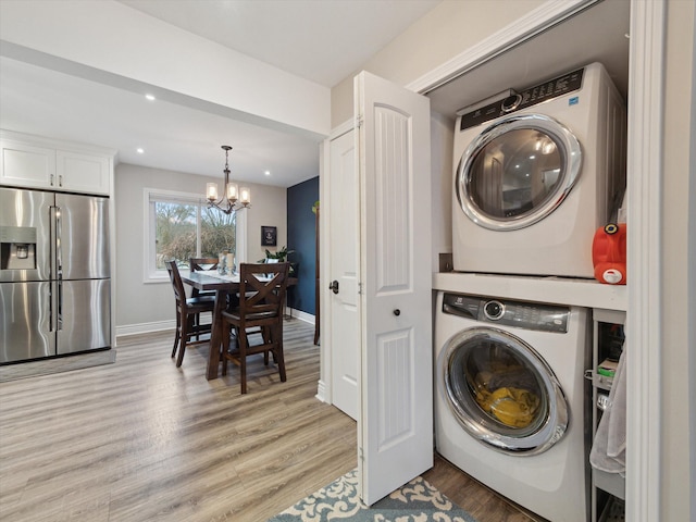 washroom featuring an inviting chandelier, stacked washer / dryer, and light wood-type flooring