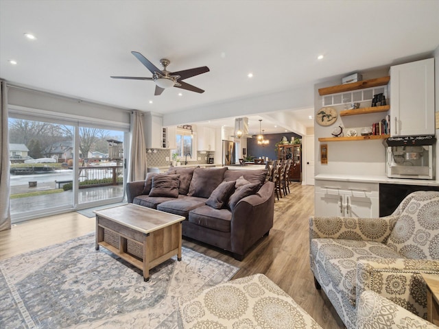 living room with ceiling fan with notable chandelier, sink, and light hardwood / wood-style flooring