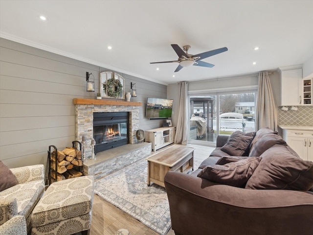 living room featuring a stone fireplace, wood walls, crown molding, light wood-type flooring, and ceiling fan