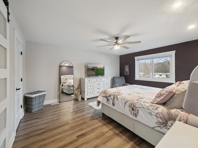 bedroom with a barn door, dark hardwood / wood-style floors, and ceiling fan