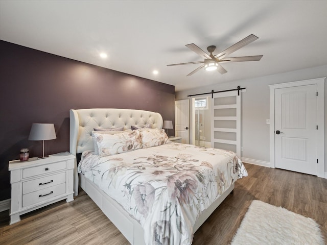 bedroom with hardwood / wood-style flooring, ceiling fan, and a barn door