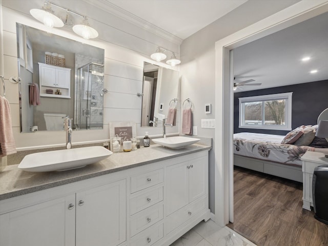 bathroom featuring a shower with shower door, vanity, ceiling fan, toilet, and crown molding