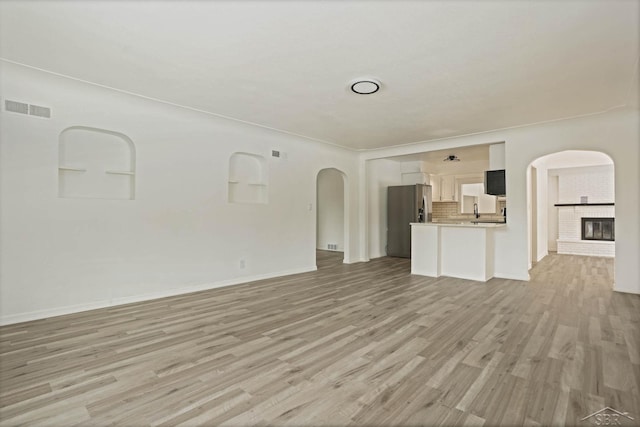 unfurnished living room featuring a brick fireplace and light wood-type flooring