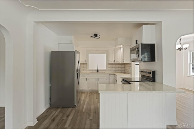 kitchen with sink, kitchen peninsula, stainless steel appliances, decorative backsplash, and white cabinets