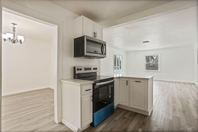 kitchen with appliances with stainless steel finishes, white cabinets, a chandelier, kitchen peninsula, and light hardwood / wood-style flooring