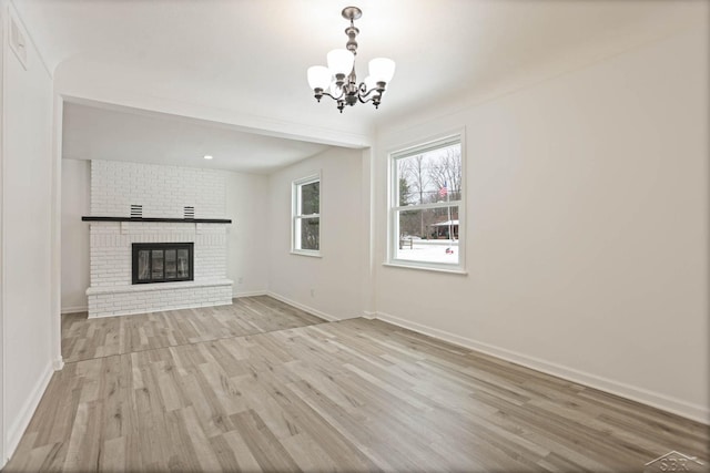 unfurnished living room with an inviting chandelier, a fireplace, and light wood-type flooring