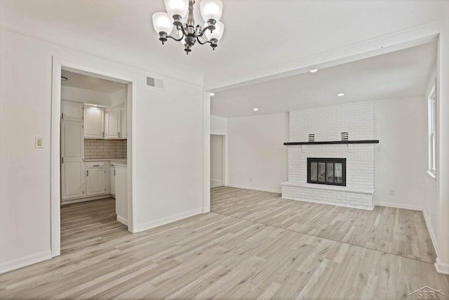 unfurnished living room featuring a notable chandelier, a fireplace, and light wood-type flooring