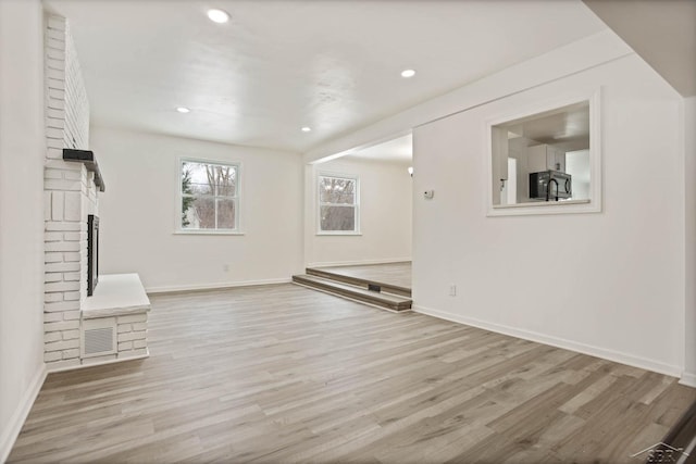 unfurnished living room featuring a brick fireplace and light hardwood / wood-style flooring