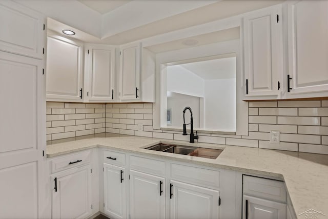 kitchen with light stone counters, sink, backsplash, and white cabinets