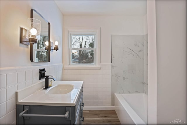 bathroom featuring hardwood / wood-style flooring, a tub to relax in, vanity, and tile walls