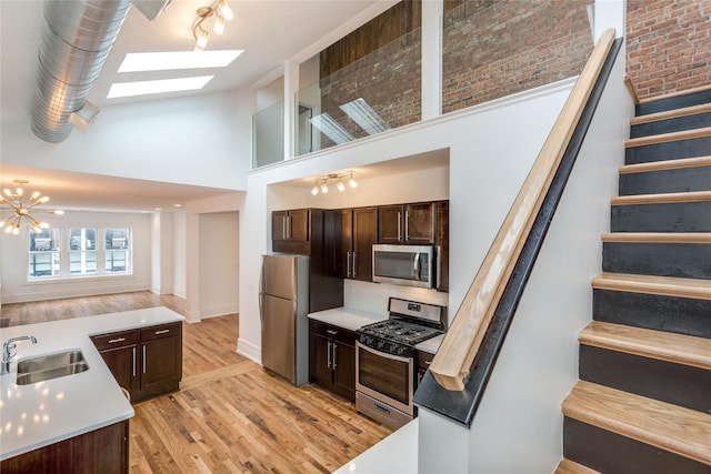 kitchen with appliances with stainless steel finishes, a skylight, sink, light hardwood / wood-style floors, and dark brown cabinetry