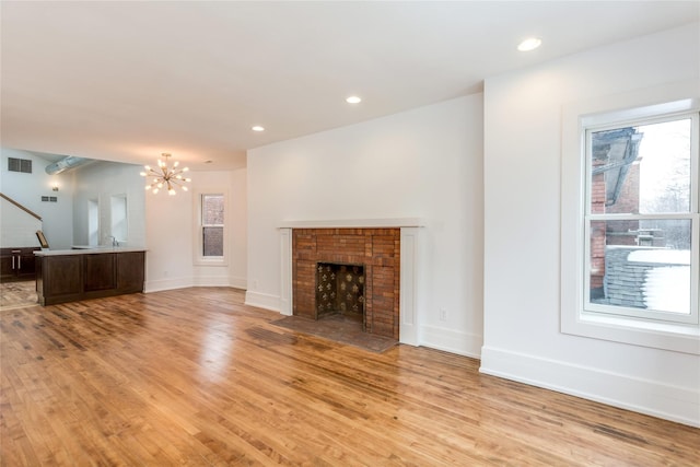 unfurnished living room with a notable chandelier, a fireplace, and light wood-type flooring