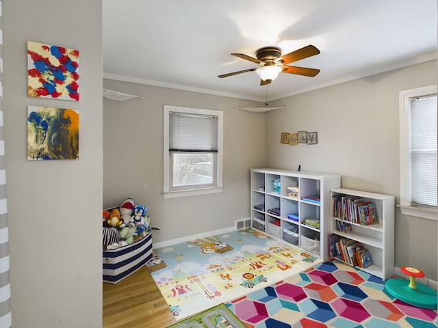 rec room with ceiling fan, baseboards, wood finished floors, and ornamental molding