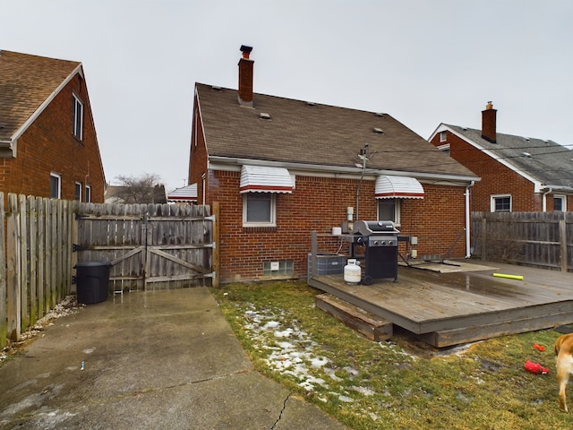 back of property with a gate, roof with shingles, a wooden deck, fence private yard, and brick siding