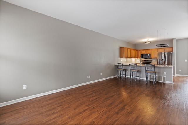 kitchen featuring appliances with stainless steel finishes, dark hardwood / wood-style floors, a kitchen bar, and kitchen peninsula