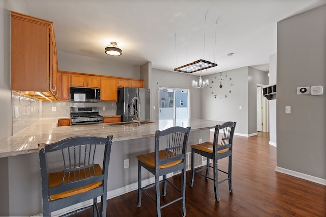 kitchen with dark wood-type flooring, a breakfast bar, appliances with stainless steel finishes, backsplash, and kitchen peninsula