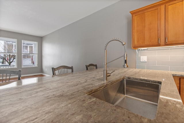 kitchen featuring sink, backsplash, a breakfast bar area, and light stone countertops