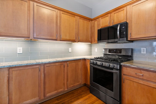 kitchen featuring stainless steel appliances, hardwood / wood-style flooring, light stone counters, and decorative backsplash