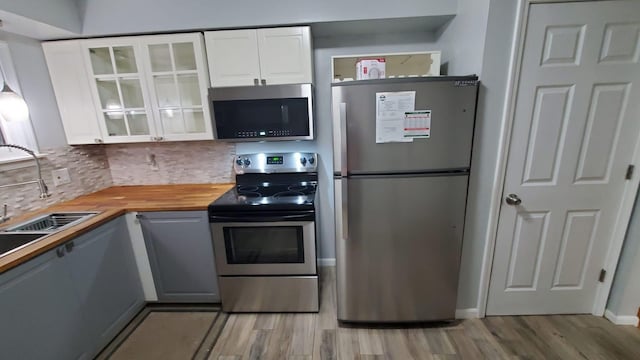 kitchen featuring butcher block countertops, appliances with stainless steel finishes, backsplash, light hardwood / wood-style floors, and white cabinets