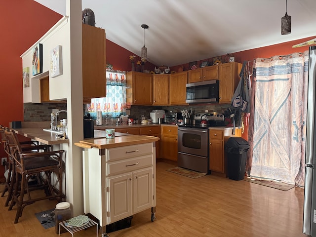 kitchen featuring lofted ceiling, light hardwood / wood-style flooring, appliances with stainless steel finishes, backsplash, and decorative light fixtures