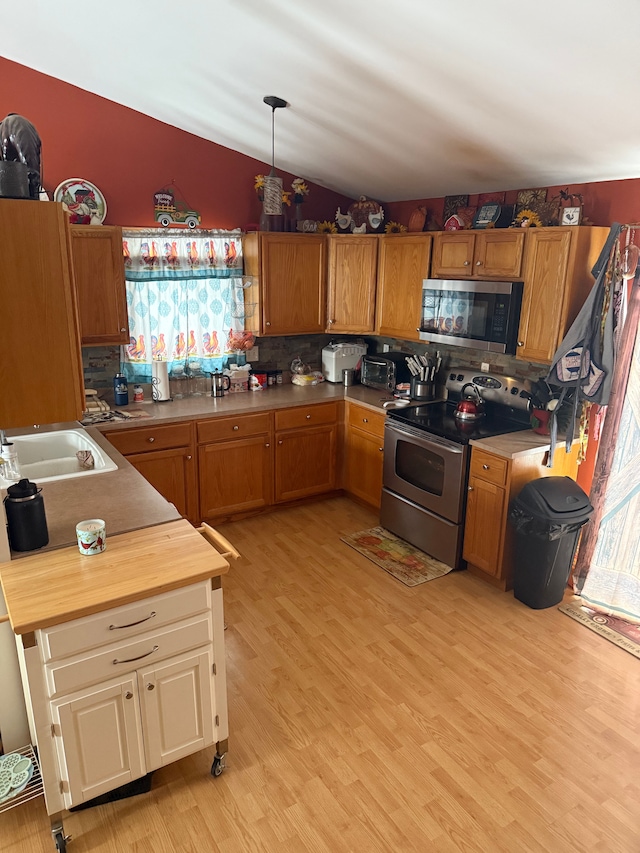 kitchen featuring vaulted ceiling, appliances with stainless steel finishes, decorative light fixtures, decorative backsplash, and light hardwood / wood-style floors