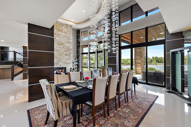 tiled dining area with a water view, a stone fireplace, a chandelier, and a high ceiling