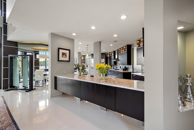 kitchen with light stone countertops, kitchen peninsula, light tile patterned floors, and decorative light fixtures