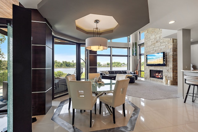 tiled dining space with a tray ceiling and a fireplace