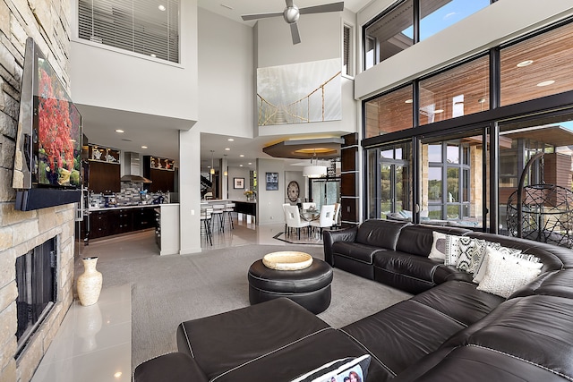 living room with a stone fireplace, carpet floors, ceiling fan, and a towering ceiling