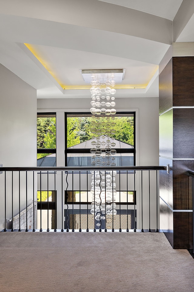 hallway with an inviting chandelier, a tray ceiling, and carpet flooring