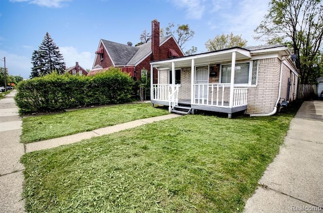 view of front of property featuring a chimney, a porch, a front lawn, and brick siding