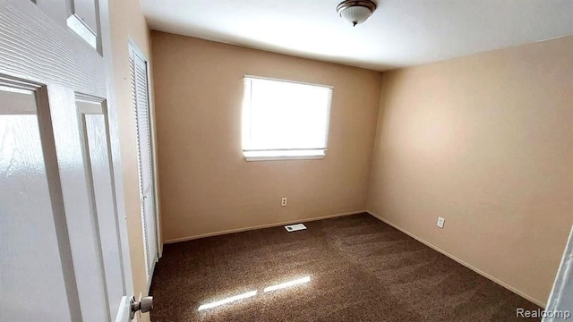 unfurnished room featuring visible vents, baseboards, and dark carpet