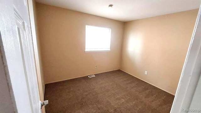 spare room featuring visible vents and dark colored carpet