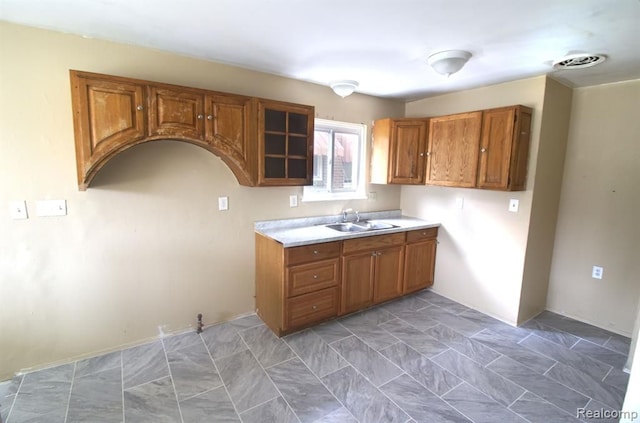kitchen with a sink, light countertops, brown cabinetry, and visible vents