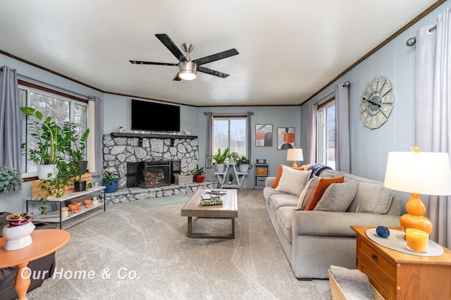 living room with ceiling fan, ornamental molding, a stone fireplace, and carpet