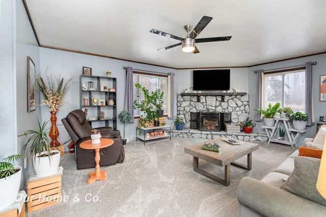 living room featuring crown molding, ceiling fan, carpet floors, a textured ceiling, and a stone fireplace