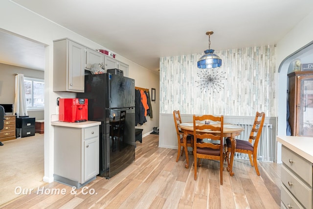 kitchen featuring black refrigerator, decorative light fixtures, gray cabinetry, and light wood-type flooring