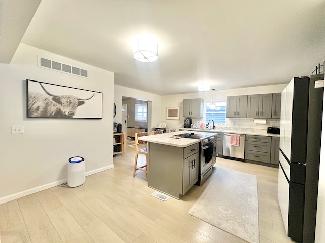 kitchen with sink, gray cabinetry, a center island, hanging light fixtures, and stainless steel appliances