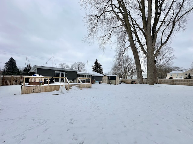 yard layered in snow with a wooden deck and a storage shed