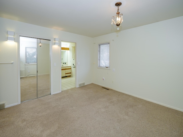 unfurnished bedroom with light colored carpet, a chandelier, and ensuite bathroom