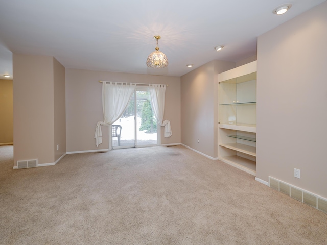 carpeted spare room featuring built in shelves and a chandelier