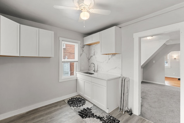 kitchen with radiator, white cabinetry, sink, decorative backsplash, and light hardwood / wood-style flooring