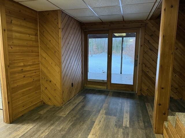 empty room with dark wood-type flooring, a paneled ceiling, and wooden walls