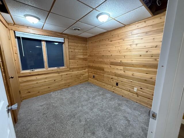 carpeted empty room featuring a paneled ceiling and wood walls