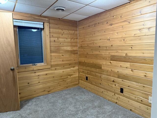 unfurnished room featuring a paneled ceiling, carpet, and wood walls