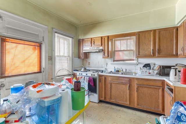 kitchen featuring brown cabinets, white gas range, light countertops, under cabinet range hood, and a sink