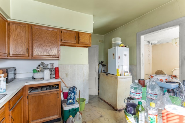 kitchen with brown cabinetry, light countertops, and freestanding refrigerator